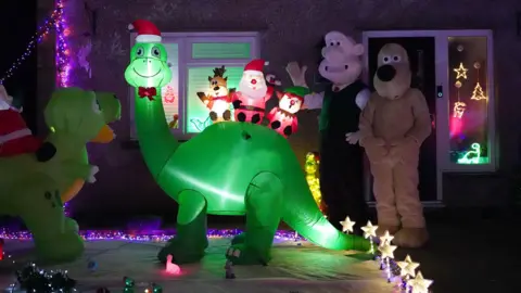 PA Media Rory's parents have created a dinosaur-themed Christmas lights display at their home to raise money for the Grand Appeal. Two blown up dinosaurs can be seen outside the house. Dressed up Wallace and Gromit stand next to the display. 