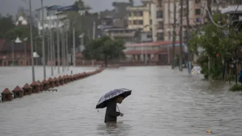 EPA A person wades through a flooded street caused by the swollen Bagmati River after torrential rains in Kathmandu, Nepal, 6 July 2024. 