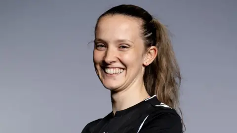 FAW Headshot photo of Ceri Williams. She has mousy brown hair pulled back in a high ponytail and smiles showing her teeth.