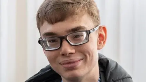 Kelvin Jay-Wakefield A young man wearing glasses with light hair smiling at the camera. 