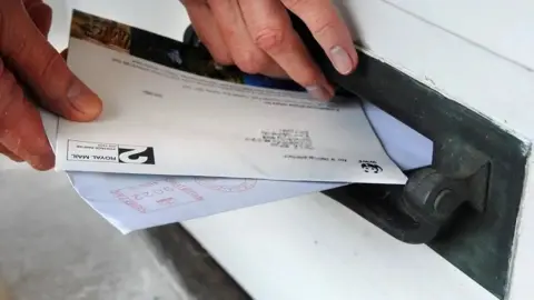 PA Media File photo of hand putting letters into a black letter box that is close to ground level.