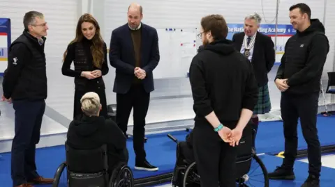PA Media The prince and princess stand in a crowd of people at the curling rink chatting. 