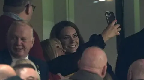 A fan taking a selfie with the Princess of Wales in a stand in the Principality stadium. Catherine is smiling. 