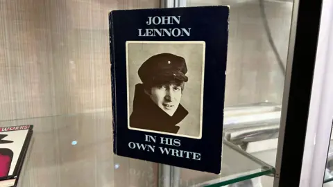 A book on a glass shelf with a photo of John Lennon on the front.