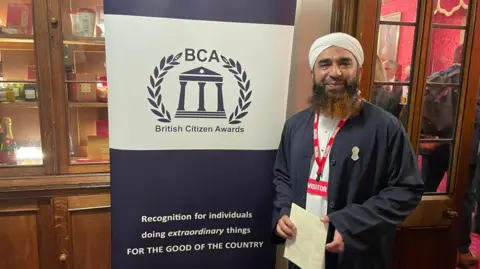 Sameer Hussain Syed Muhammad Faisal Sami stood by a British Citizen Awards banner