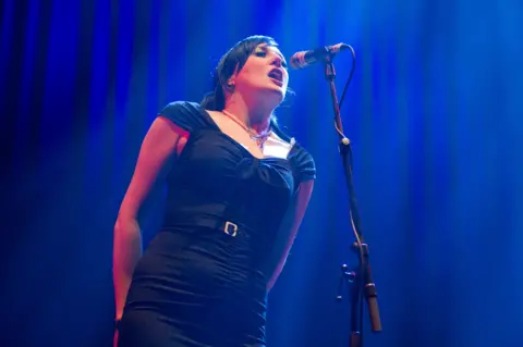 Getty Images Lou Hickey sings onstage - she has dark hair and is wearing a black dress.