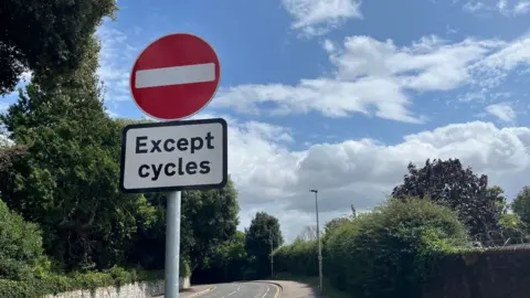 A red and white no entry sign above a sign saying 'Except cycles' marking the beginning of the section of road on Dryden Lane in Exeter that is closed to cars.