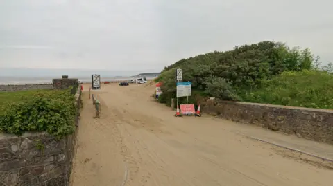 A road leading to a sandy beach in Weston-super-Mare. There are some signs and cones at the entrance