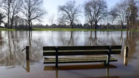 PA Media A bench in a flooded open green space area in Datchet. It is sunny.