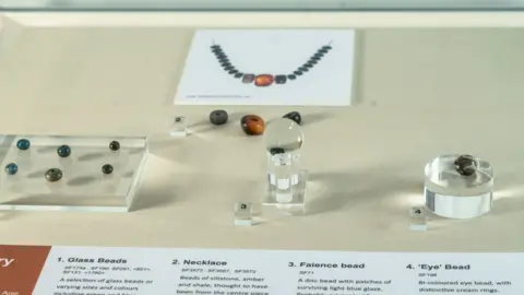 Martin Rowe/Peterborough Museum and Art Gallery View of Bronze Age beads on display, including blue/green glass beads, a faience bead and a photograph of a replica of a necklace at Peterborough Museum