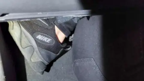 HomeOffice A woman's foot covered in a black Nike trainer sticks out from the glove compartment of a car. 