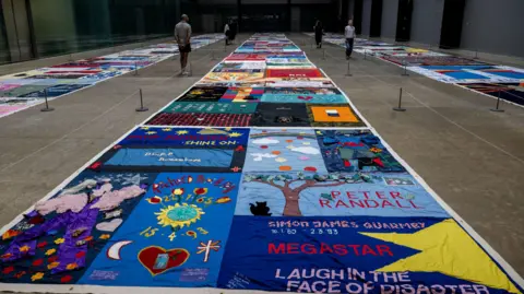 Reuters Closer image of a section of the UK AIDS quilt shows some of the individual submissions. One has a large tree and a cat, another the name of its subject and a quote, and another has some appropriate symbols.