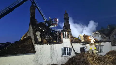 Firefighters tackling a fire at a gutted thatched roof cottage