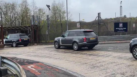 Three black cars driving into the entrance of the Faslane nuclear base. 