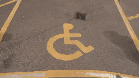 An empty disabled car parking bay with yellow markings, including the wheelchair symbol.