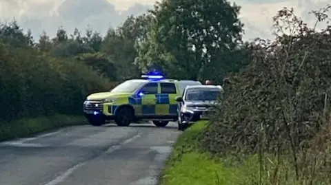 Submitted A police car and a truck parked down a country lane near Cirencester in Gloucestershire