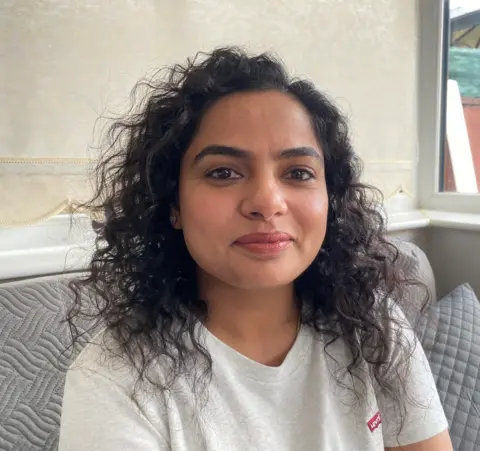 Mrs Raman Kaur is a young woman who is wearing a grey t-shirt. She has black curly hair. 