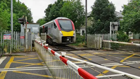 A train is crossing a railway line which has red and white barriers across the road. There are markings on the road.