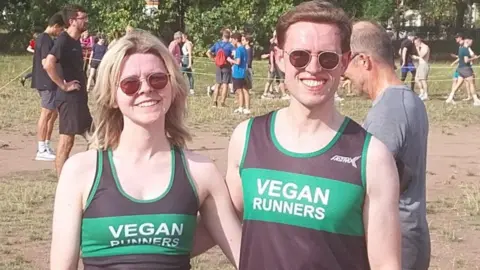 Laura Murphy Laura Murphy and Niall Robb are both wearing running vests that say Vegan Runners on the front in white text on a green strip running across a black backround. The woman has blonde hair and the man brown hair. They are both wearing sunglasses. Other runners can be seen in the background.