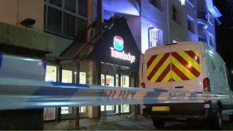 Police tape and a police van outside a Travelodge hotel at night