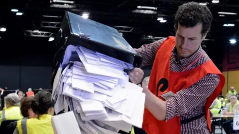 Man pores a box of votes onto a table 