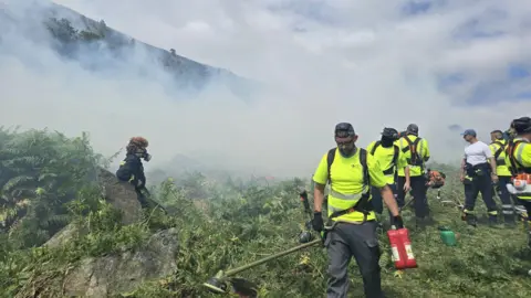 DFRS A group of firefighters, most wearing masks, with lots of smoke in the air