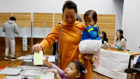 Reuters Una donna vestita in costume di Halloween con i suoi figli vota alle elezioni generali in un seggio elettorale a Tokyo, in Giappone, il 27 ottobre 2024.