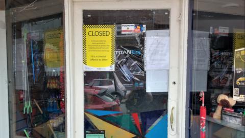 Sign saying 'closed' on the front of a shop window, next to it is a copy of the closure order attached to the window