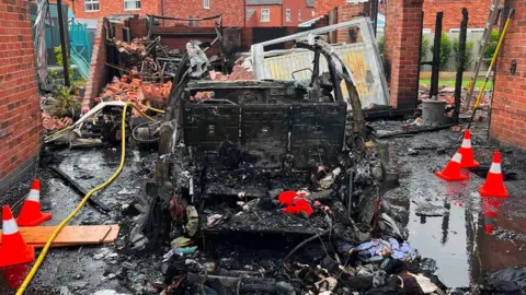 Leicestershire Fire and Rescue Service A burnt out car with a damaged building behind the vehicle
