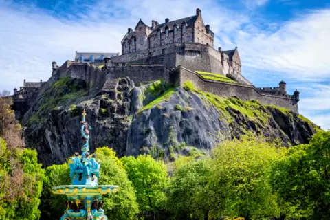 Getty Images A view of Edinburgh Castle on a sunny day. The Ross Fountain is in the foreground and the netting over the rockface of the castle is visible in the background. 