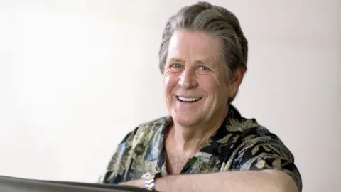 Brian Wilson pictured with one arm leaning on a piano in the early 2000s