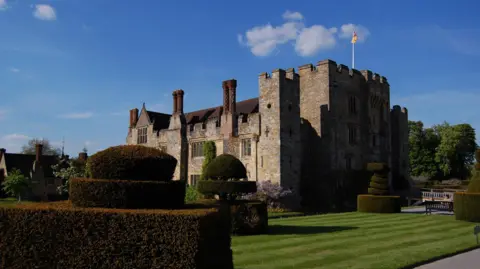 Hever Castle, a stone manor house, surrounded by a manicured garden on a sunny day.