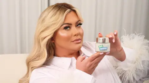 Gemma Collins, who is blond and looking seriously at the camera. She is holding a pot of anti-ageing cream that reads: "Face forward".