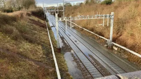 BBC A view of a railway line with flood water on it. 