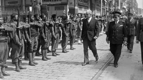 An archive black-and-white archive shot of African troops being inspected by French officials.