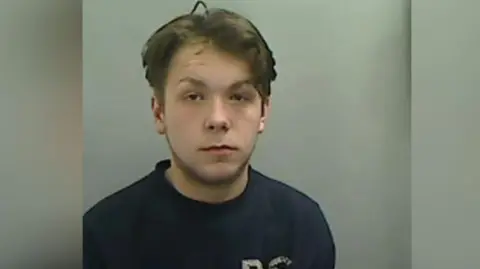 Mugshot of a Dominic Legg. He has short dark hair and is wearing a dark blue top.