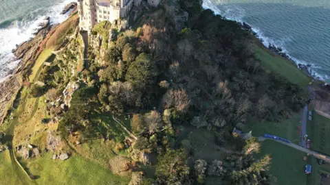 Henry Mathews An aerial image of St Michael's Mount. There is a large building to the top of the image, alongside fallen trees.