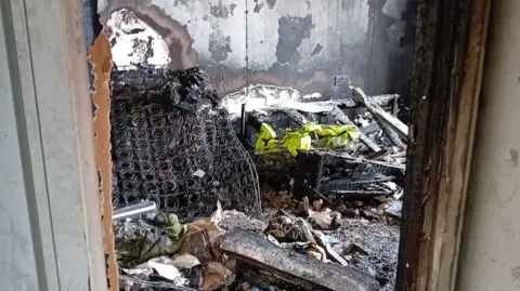 Nabeel Ahmad The wreckage of the fire in a room in Nabeel Ahmad's flat, including a burned out bed, from which the exposed metal of a mattress is shown. 