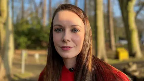 Emma is pictured wearing a red jumper with trees in the background