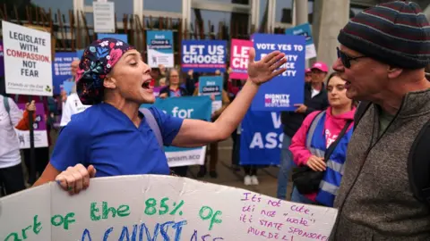 Doctor Geri Hignett (left) protests against the proposed law on assisted dying outside the Scottish Parliament. A large group of pro-assisted dying demonstrators are in the background.