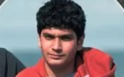Nischay Patel had short, wavy black hair and wore a red hooded top, while standing in front of the sea.