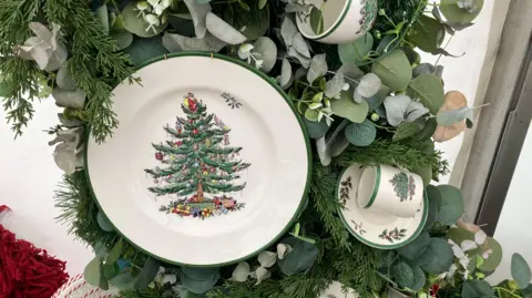 A close-up of a plate, mug and saucer each with Christmas trees and holly designs on them