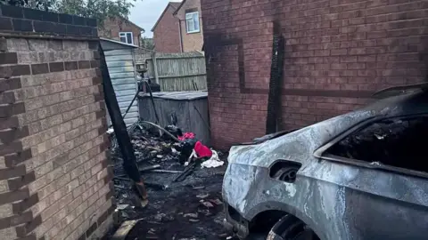 Facebook The remains of a car which was engulfed in flames. What is left of the car is charred and there is damage to the back of the property.