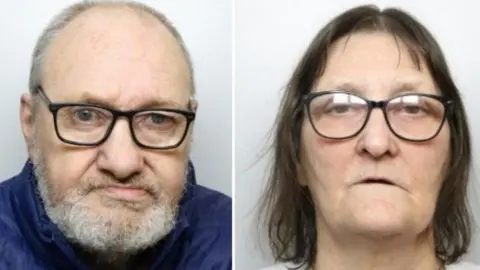 A police mugshot of a 66-year-old man with a grey beard and hair wearing a blue puffa jacket and black glasses, next to a police mugshot of a 64-year old woman with brown hair, a grey pullover and black glasses