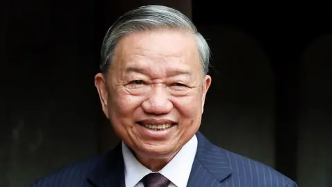 A photo of To Lam smiling at the Temple of Literature in Hanoi on May 26, 2025. He is wearing a dark striped suit.