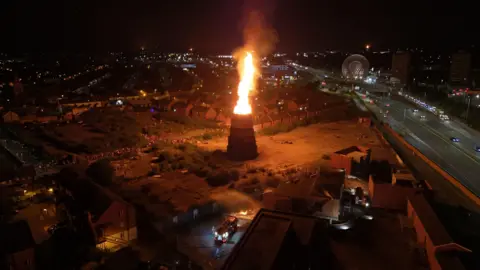 A tall bonfire close to houses lit during 11th July celebrations in 2025.