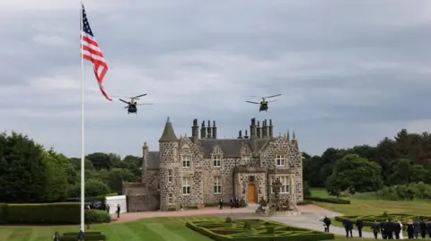 Reuters mały budynek zamku obok flagi USA, gdy dwa helikoptery wojskowe latają nad głową