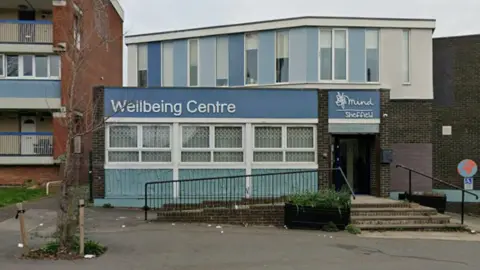 Google The exterior of a community centre. The panels are painted blue and white letter read "wellbeing centre". There is a ramp up to the door and windows on both floors.