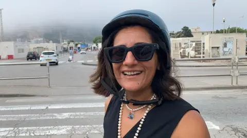 BBC Spanish woman Shilpi Chotrani who every working day travels across the border by motorbike to work in Gibraltar. She is wearing a helmet and sunglasses.