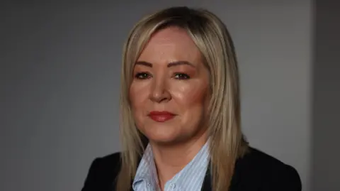 PA Media Michelle O'Neill has long blond hair and is wearing a dark suit jacket and light blur shirt 